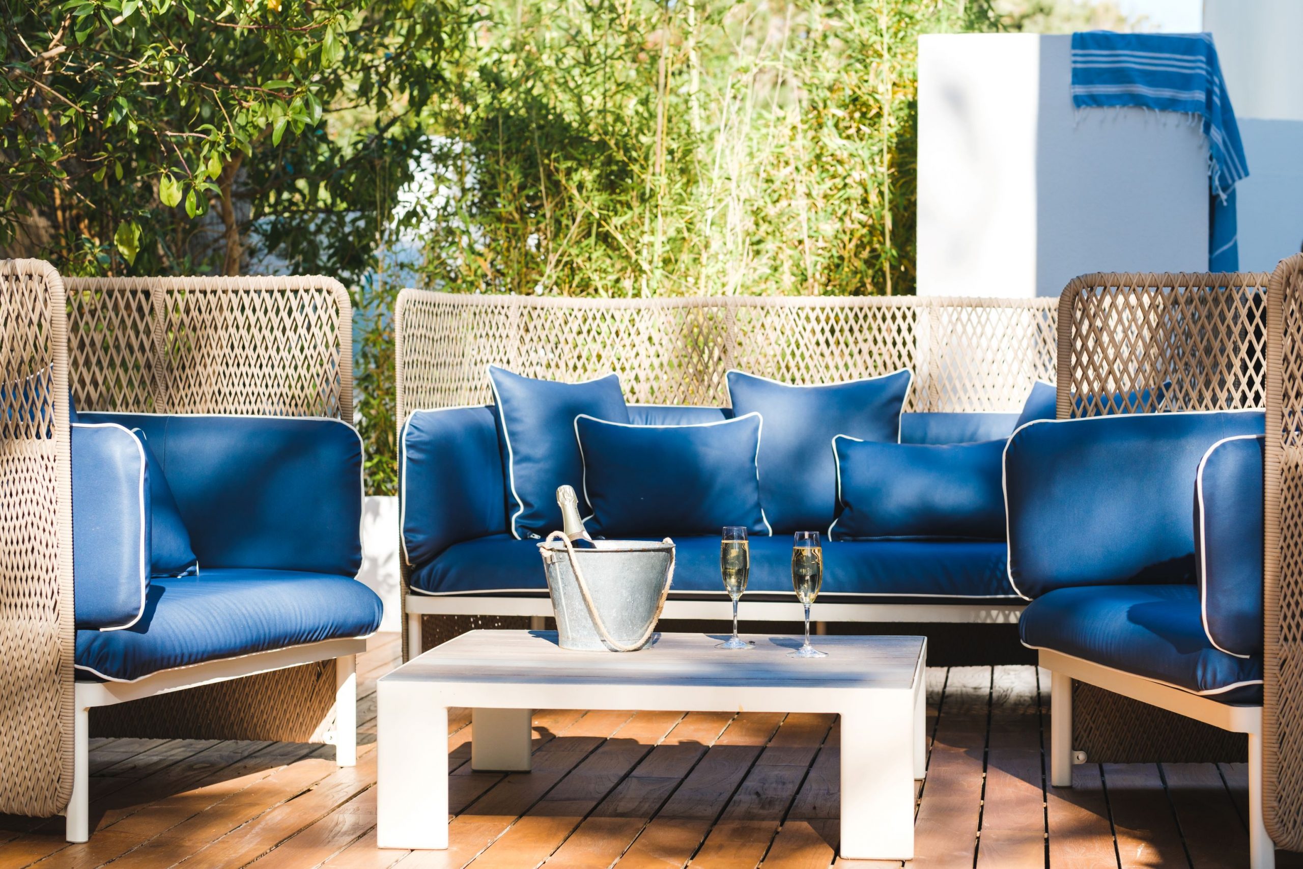 Boho loungehoek met blauwe kussens op het houten terras van Gecko Beach Club