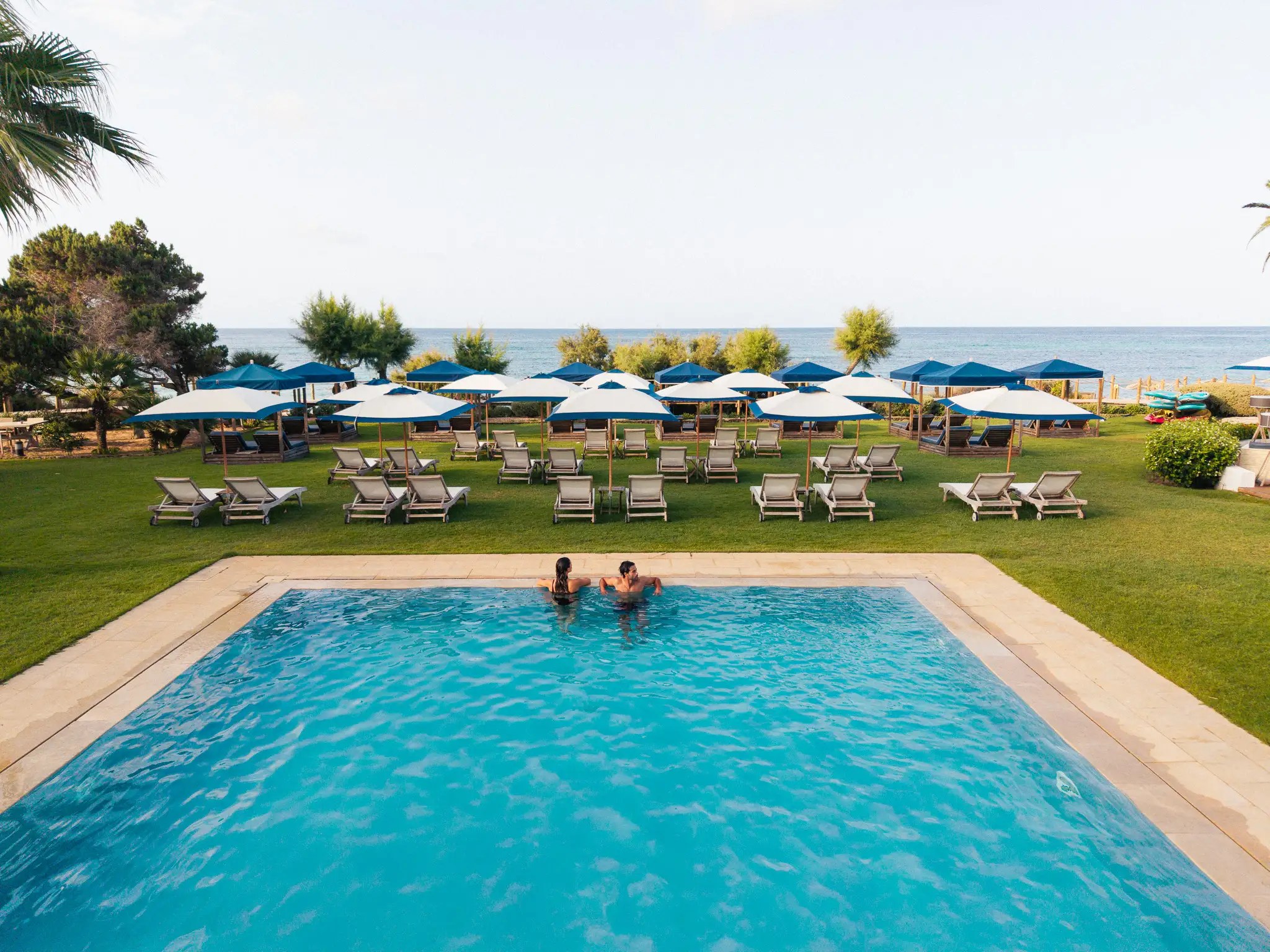 Het zwembad met ligbedden en parasols van Gecko Beach Club met de zee erachter