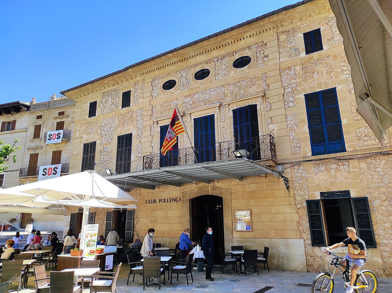 De goedkoopste maand voor de Balearen 1 Terras met gasten voor een oud pand aan het plein van Pollenca op Mallorca