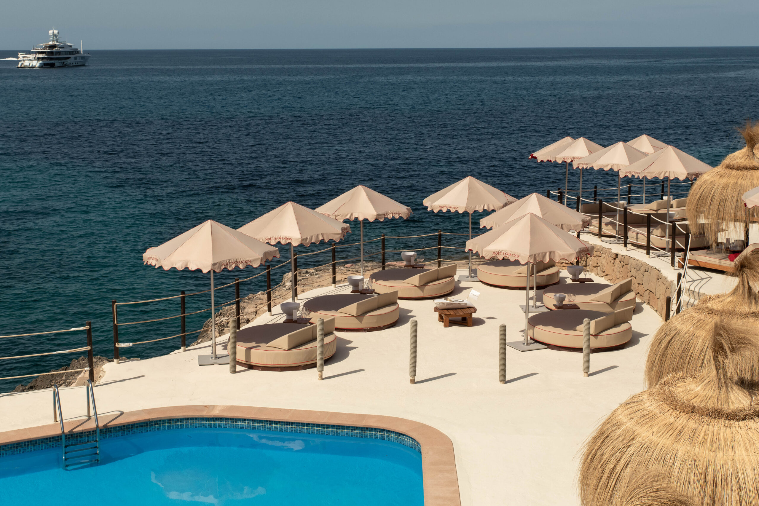Gran Folies Mallorca: cliffside beachclub boven Cala Llamp bij Port d'Andratx 2 Ronde Balinese ligbedden en parasols op het rotsterras van Gran Folies met de zee erachter