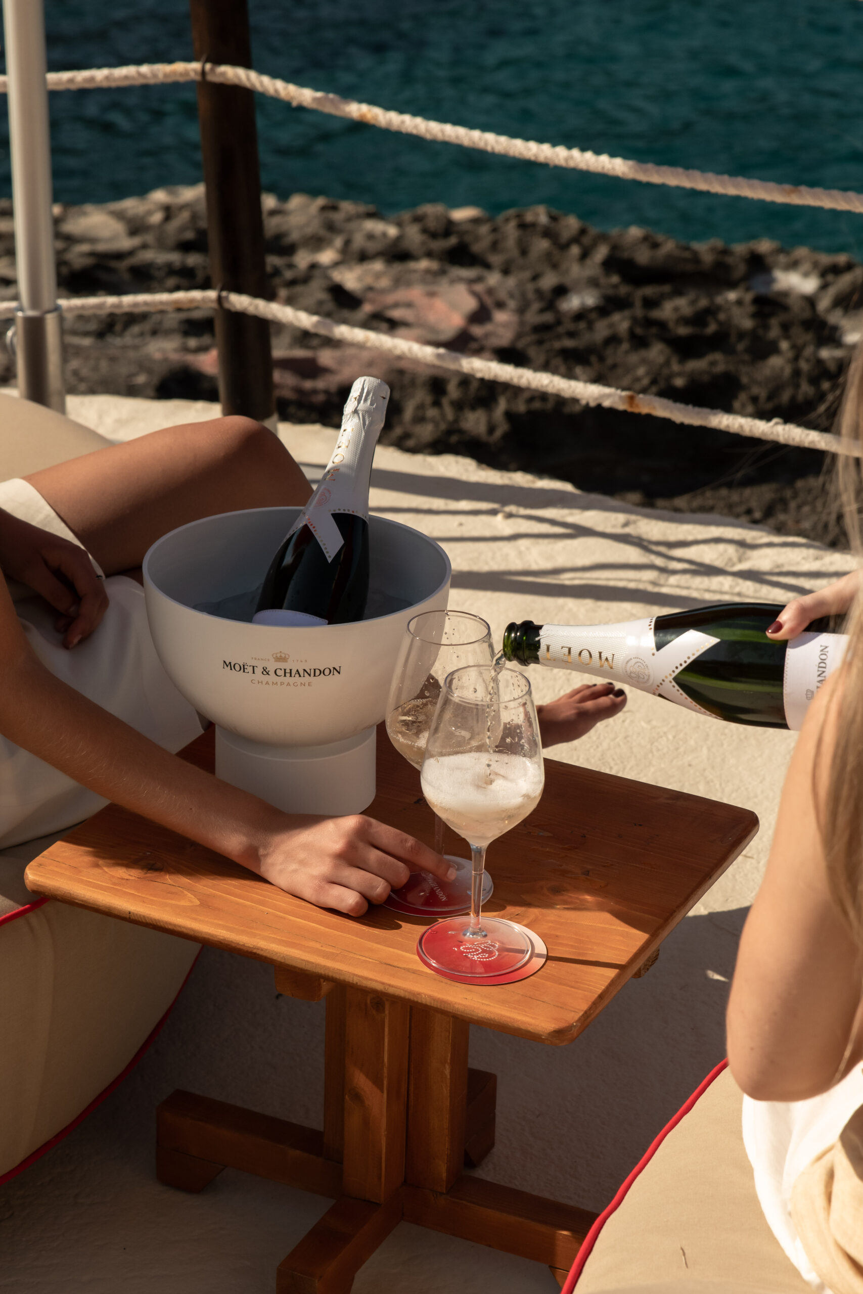 Gran Folies Mallorca: cliffside beachclub boven Cala Llamp bij Port d'Andratx 3 Champagne in een koeler en wijnglazen op een tafel op het terras van Gran Folies boven zee