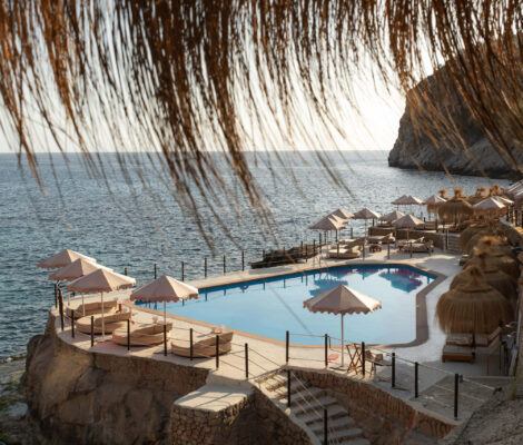 Het zwembad en de rieten parasols van Gran Folies op de klif boven Cala Llamp met de zee erachter