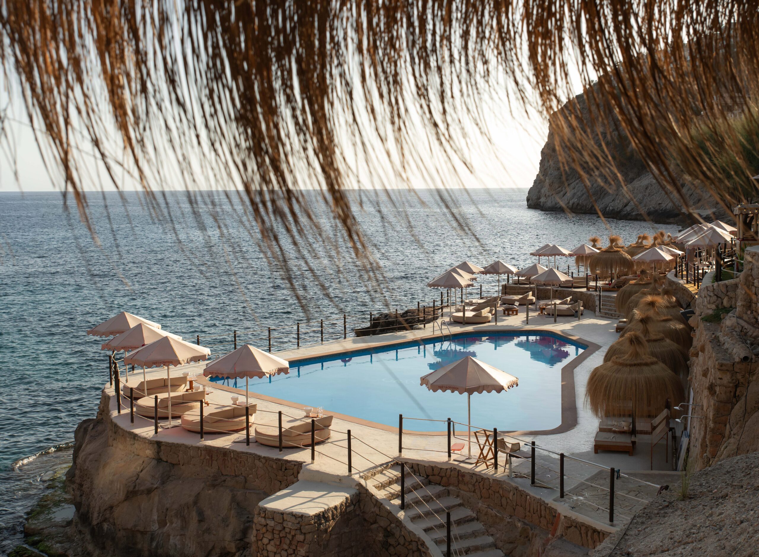 Gran Folies Mallorca: cliffside beachclub boven Cala Llamp bij Port d'Andratx 5 Het zwembad en de rieten parasols van Gran Folies met de open zee erachter