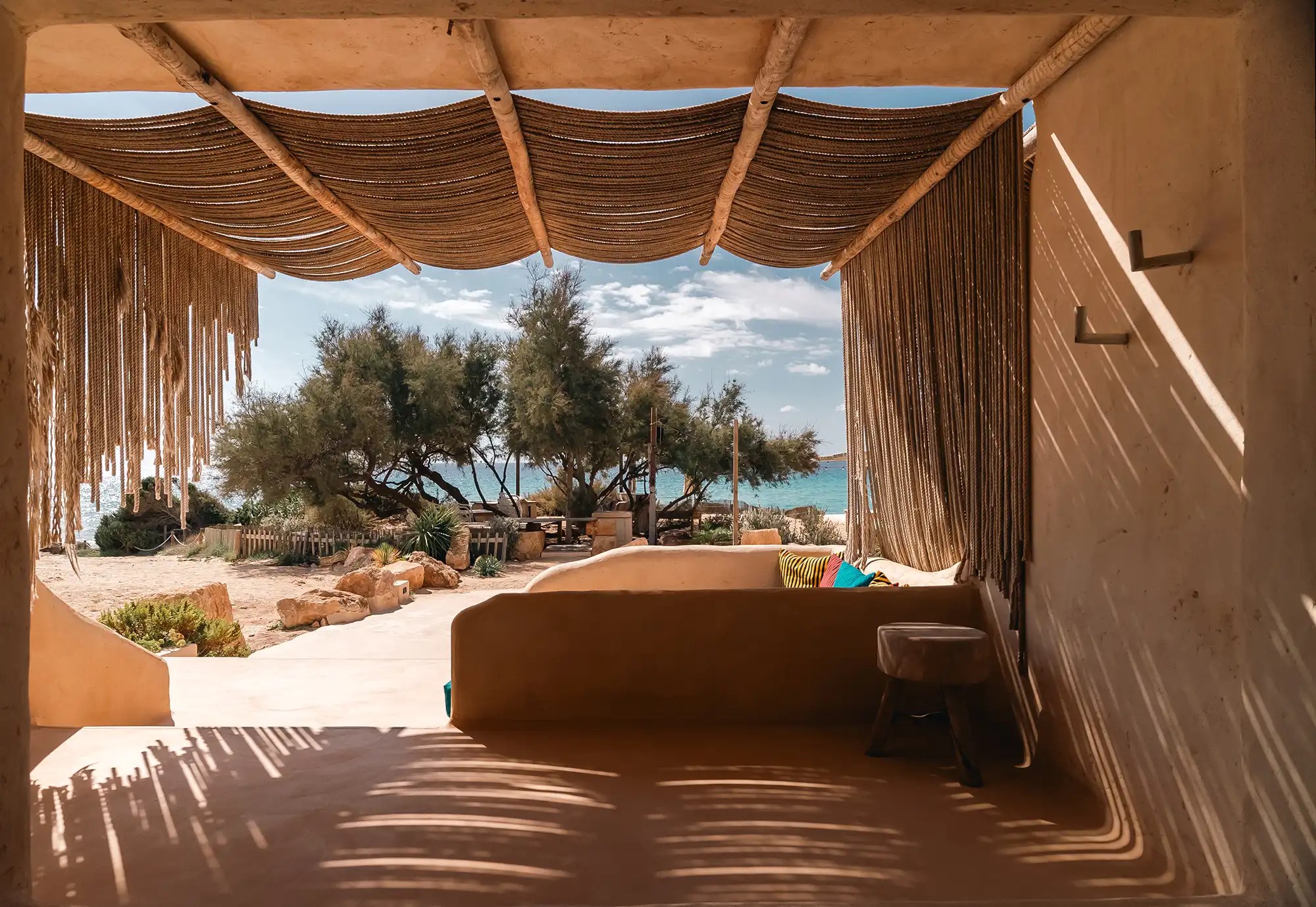 Hannah Formentera: strandrestaurant en sunset aan Es Arenals (Migjorn) 6 Loungehoek van Hannah Formentera met uitzicht op de turquoise zee door de tamarisken