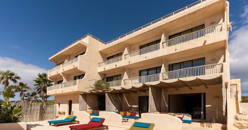 De strandgevel van Hannah Formentera met balkons en gekleurde ligbedden aan Playa de Es Arenals