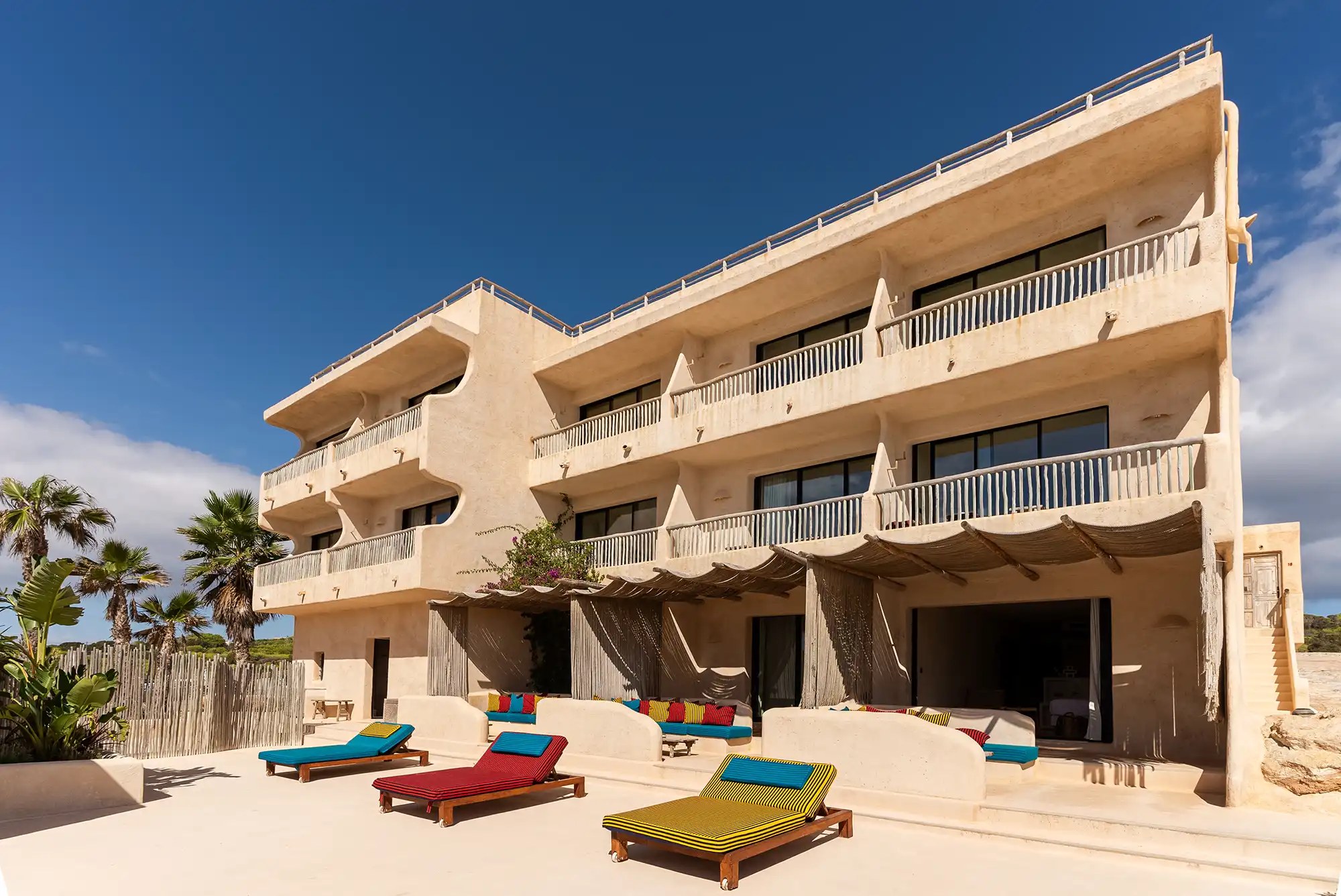 Hannah Formentera: strandrestaurant en sunset aan Es Arenals (Migjorn) 1 De strandgevel van Hannah Formentera met balkons en gekleurde ligbedden aan Playa de Es Arenals