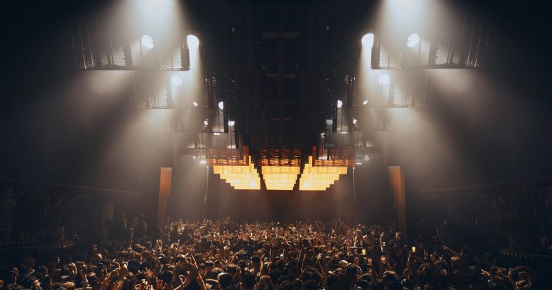 De Theatre van Hï Ibiza met spotlights boven een volle dansvloer, gezien van achter het publiek