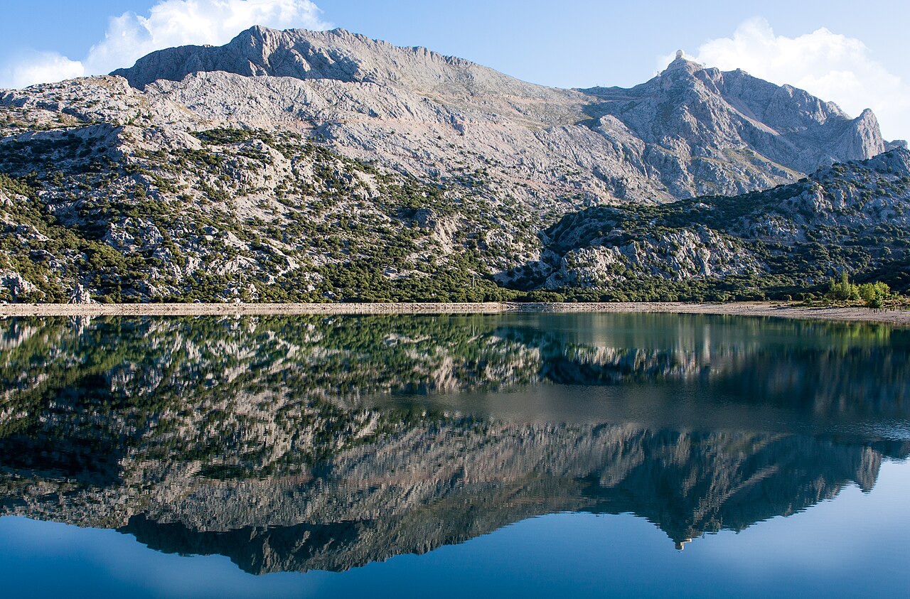 Hoe groot is Mallorca? Oppervlakte, afmetingen en rijtijden 6 Het stuwmeer Cúber aan de voet van de Puig Major op Mallorca, met de bergen weerspiegeld in het water