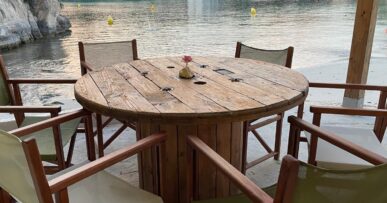 Houten strandtafel met groene regisseursstoelen op het terras van Hopi Beach Bar met de cala van Cala en Blanes erachter