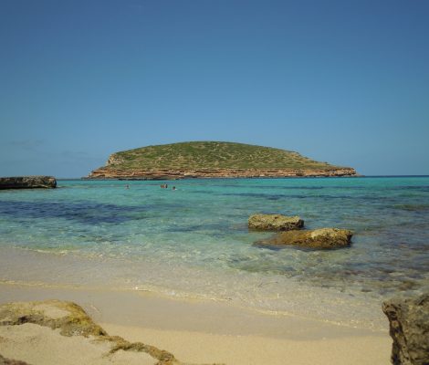 Turquoise water bij een baai op Ibiza met een groen eilandje ervoor, illustratief voor de keuze tussen Ibiza en Mallorca