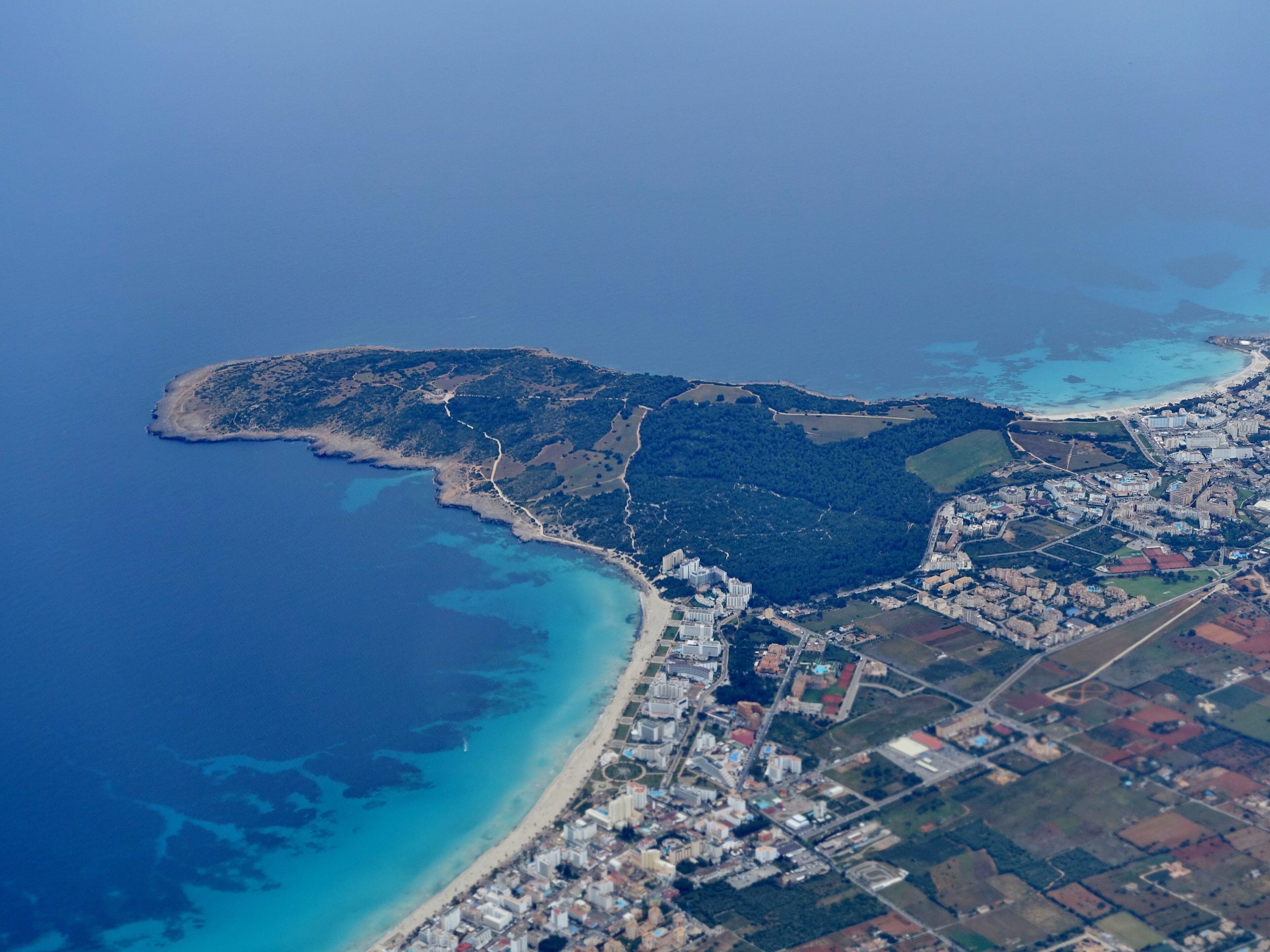 Luchtfoto van de kust van Mallorca met een breed strand, een onbebouwd schiereiland en de badplaatsen erachter