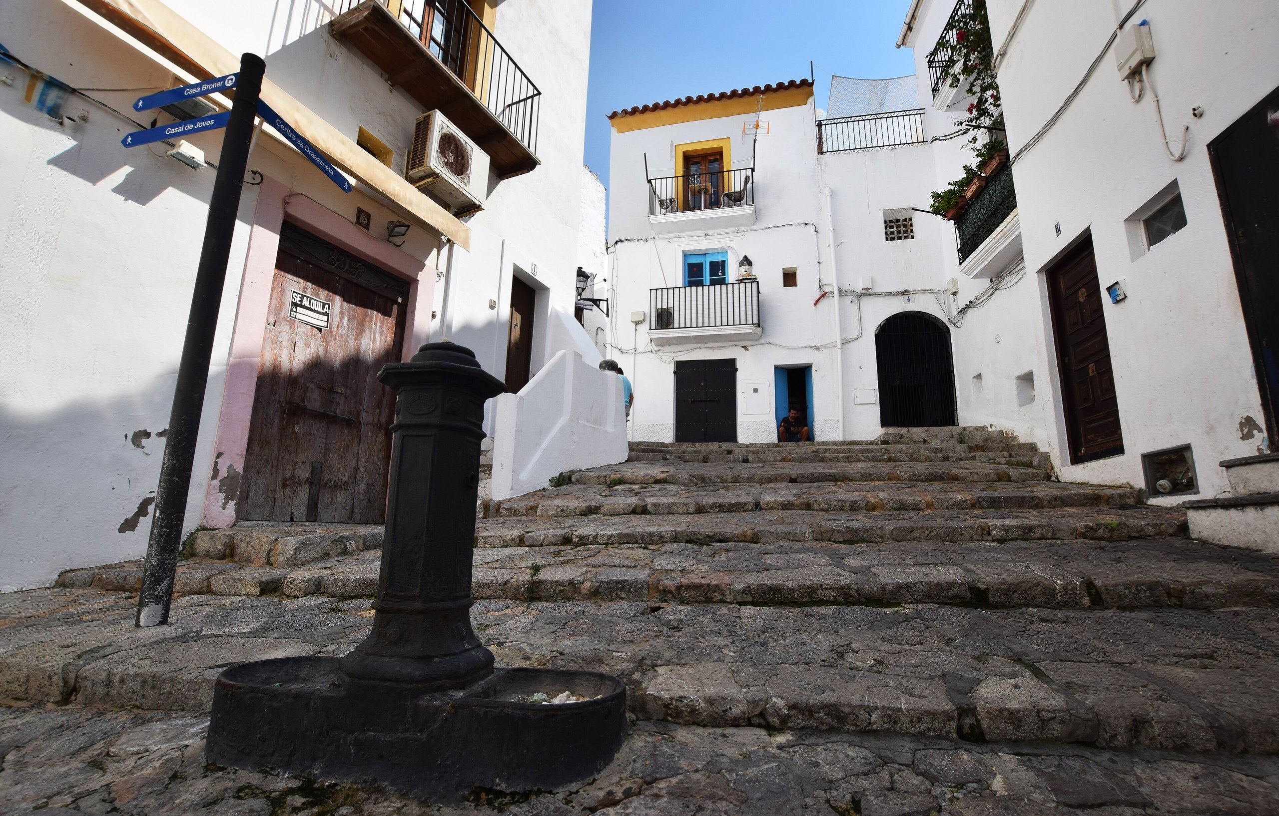 Trappenstraat Costa de sa Drassaneta in Sa Penya, Ibiza-stad, met witte huizen en een ijzeren fontein