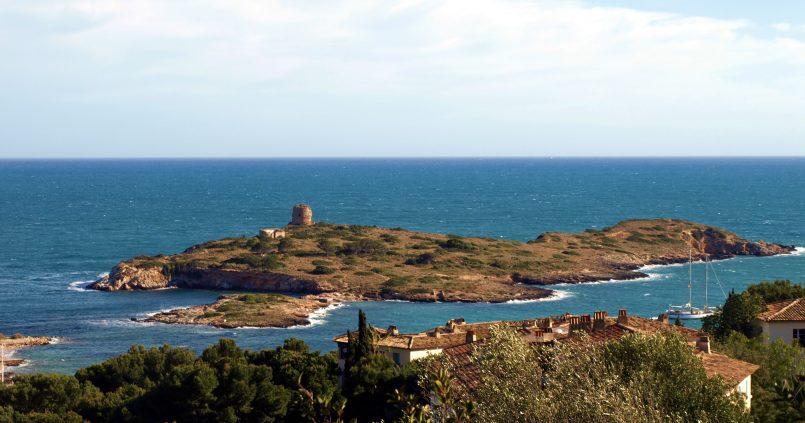 De eilandjes voor de kust van Illetes op Mallorca met de oude verdedigingstoren erop, diepblauwe zee en pijnbomen en villa's op de voorgrond