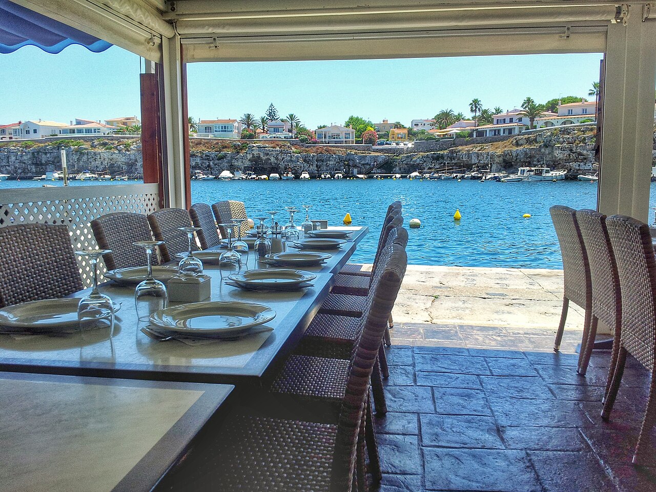 Is Menorca duur? Wat een vakantie in 2026 echt kost 7 Terras boven de vissershaven Cales Fonts in Es Castell op Menorca, met gedekte tafels aan het water