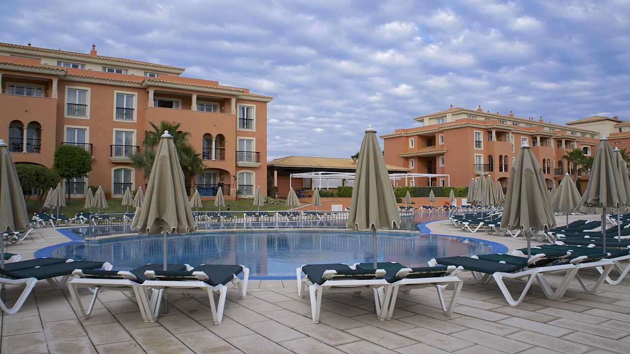 Is Menorca duur? Wat een vakantie in 2026 echt kost 6 Ligbedden en parasols rond het zwembad van een hotel op Menorca