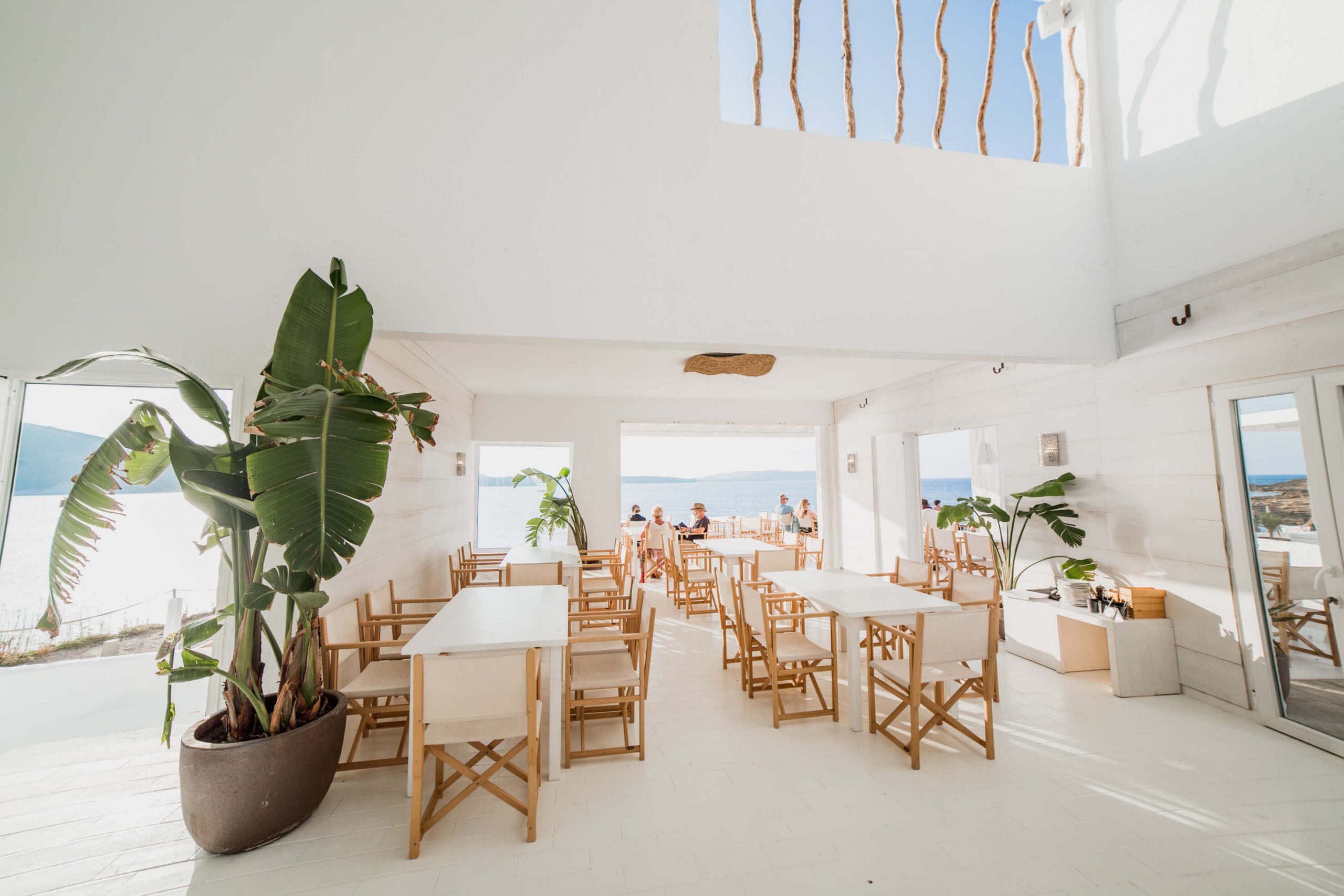 Het lichte interieur van Isabella Beach Club met houten tafels en zeezicht