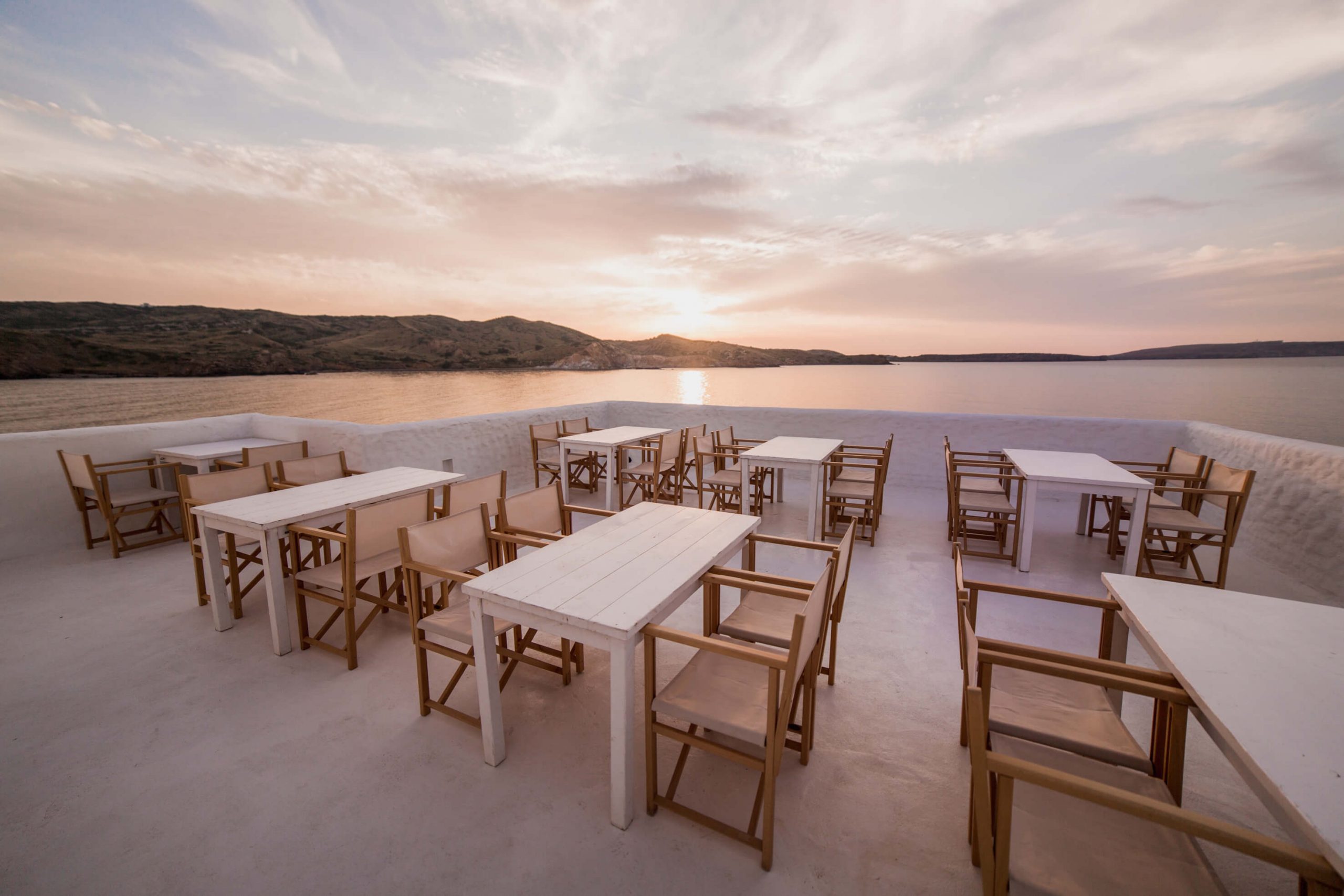 Het witte terras van Isabella Beach Club op de rotsen bij Platges de Fornells bij zonsondergang