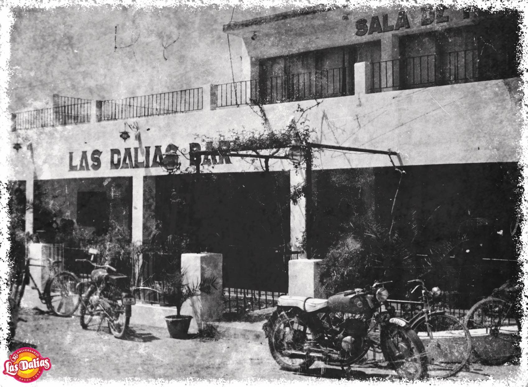 Las Dalias Ibiza: de iconische hippiemarkt van Sant Carles 2 Zwart-witfoto van de gevel van Las Dalias Bar in Sant Carles in de jaren vijftig, met fietsen en een motor voor de deur