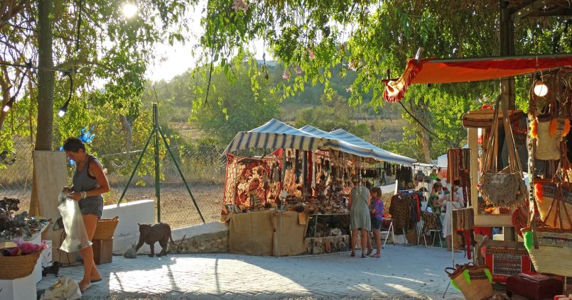Kraampjes met tassen, sieraden en textiel onder de bomen van de hippiemarkt Las Dalias in Sant Carles, Ibiza