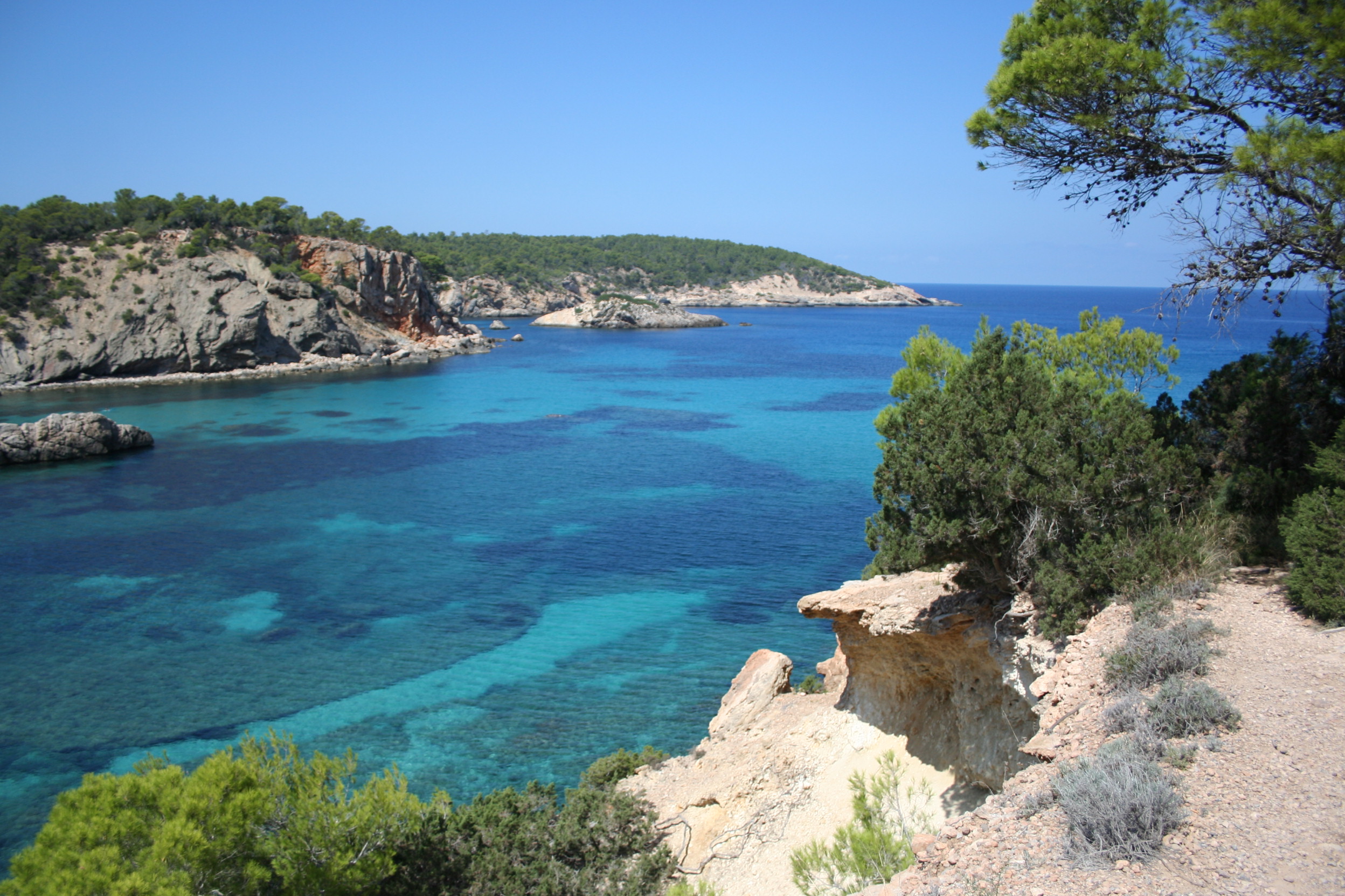 Turquoise water en rotsige kliffen met pijnbomen aan de noordkust van Ibiza bij Portinatx