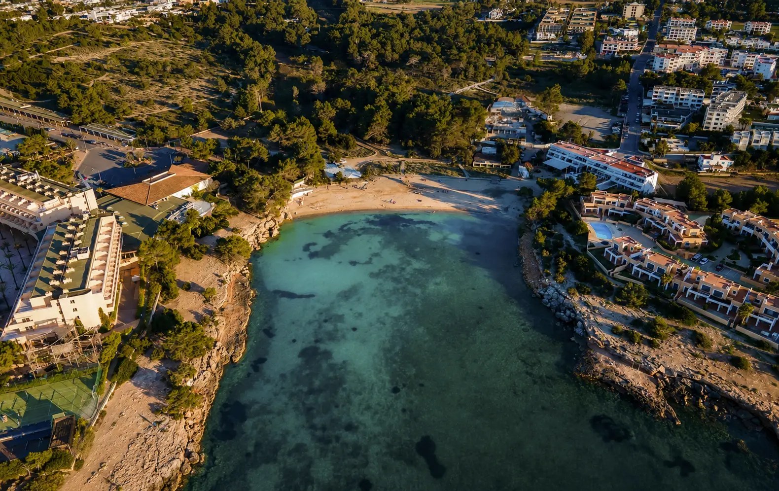Ñora Beach Ibiza: strandrestaurant en ligbedden aan Port des Torrent 1 De baai van Port des Torrent op Ibiza vanuit de lucht, met Ñora Beach aan het zand