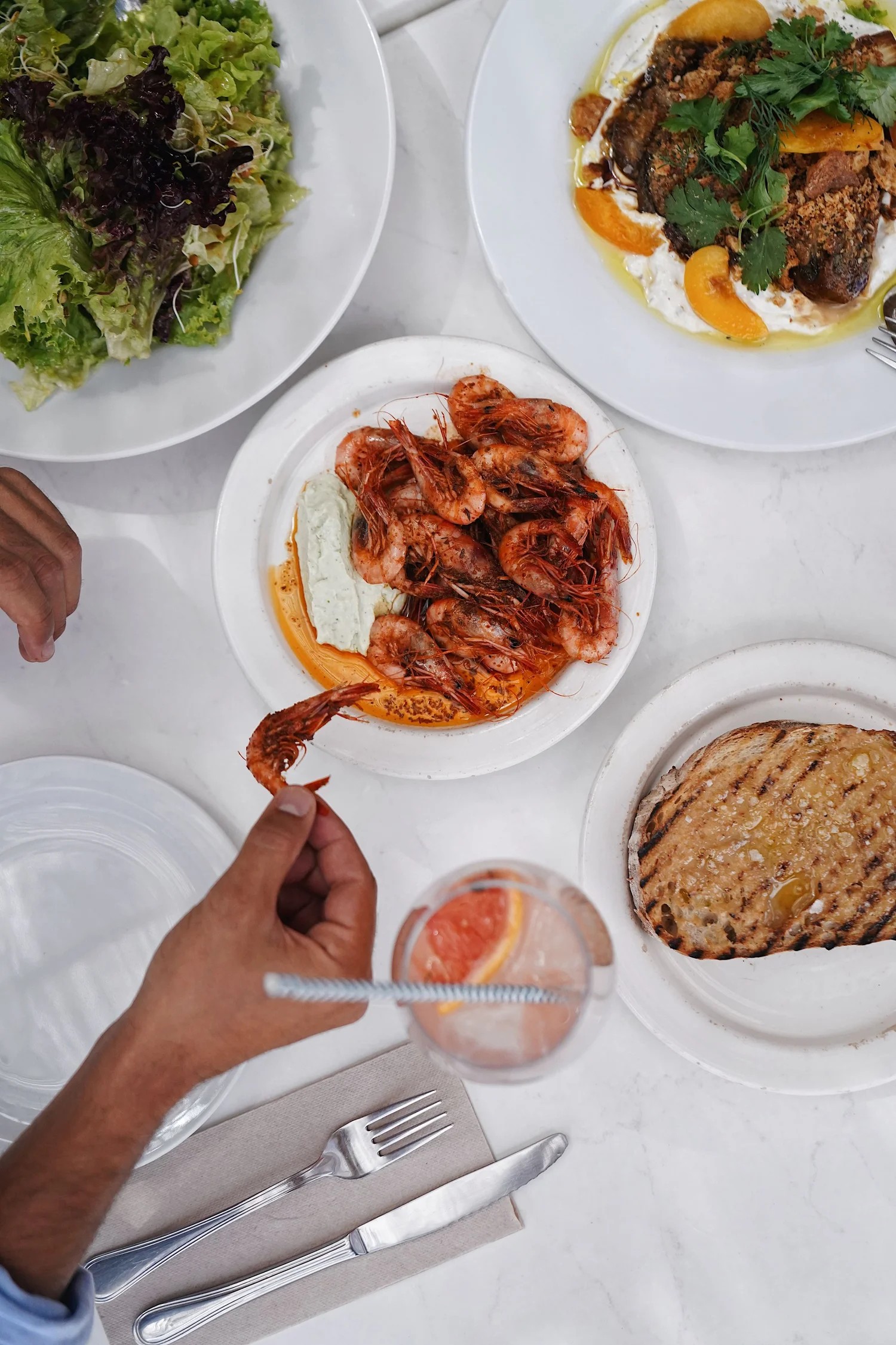 Gedekte tafel met gegrilde gamba's, brood en drankjes om te delen bij Patiki Beach