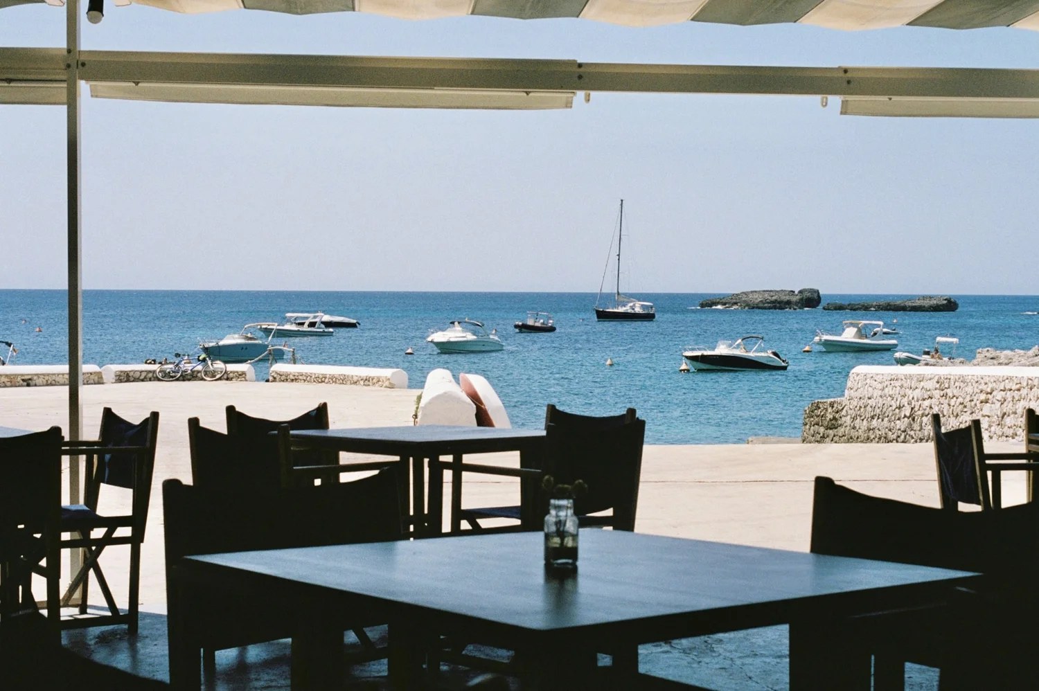 Het terras van Paupa onder het zonnescherm met uitzicht op de baai en de bootjes van Cala Torret op Menorca