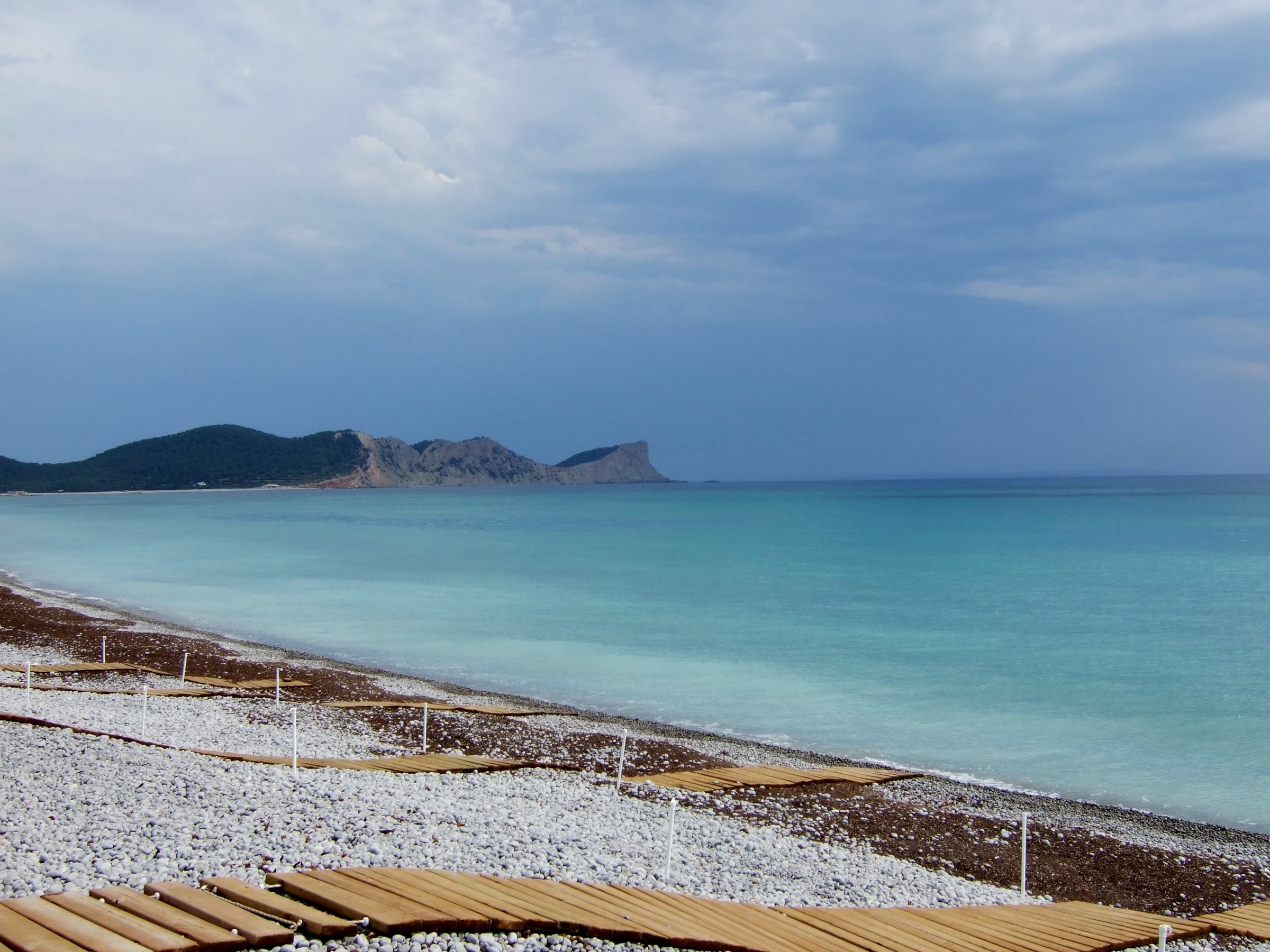 Platja des Codolar Ibiza: het langste, wildste strand van het eiland 2 Grijze kiezels en turquoise water op Platja des Codolar, met Cap des Falcó in de verte, Ibiza