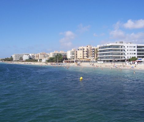 Het lange zandstrand van Playa d'en Bossa op Ibiza met hotels langs de kust en helder blauw water