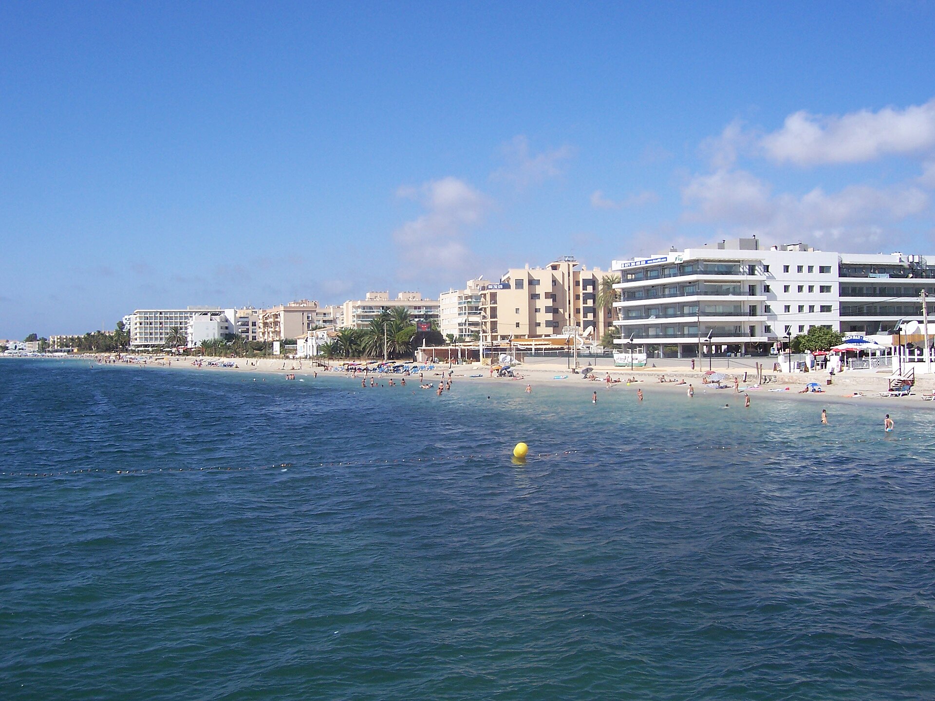 Het lange zandstrand van Playa d'en Bossa op Ibiza met hotels langs de kust en helder blauw water