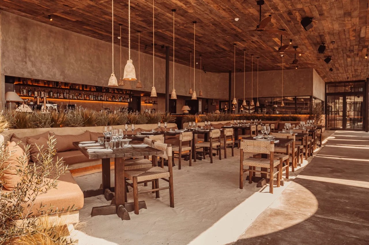 De open zaal van Playa Soleil met houten tafels en rieten kappen