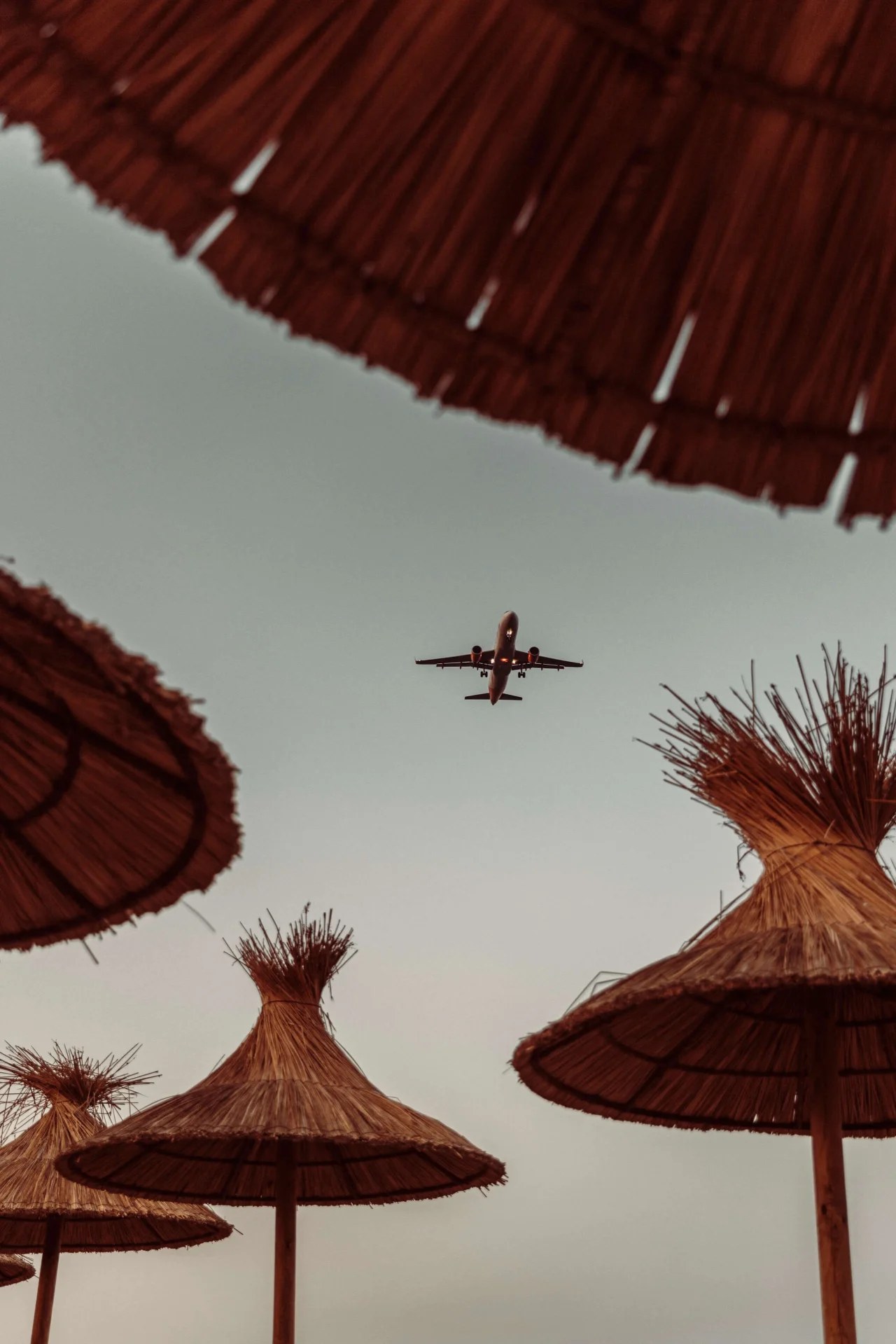 Rieten parasols bij Playa Soleil met een laagvliegend vliegtuig erboven