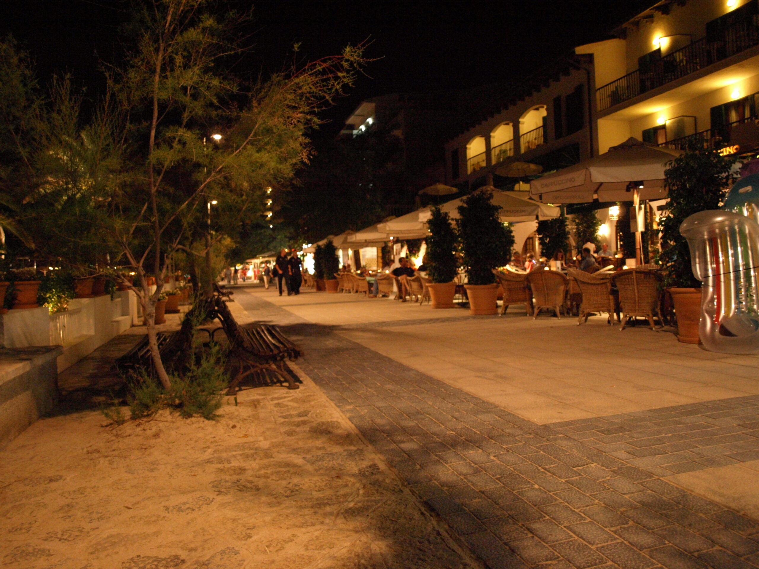 De Pine Walk in Port de Pollença in de avond, met verlichte terrassen onder de pijnbomen langs de promenade