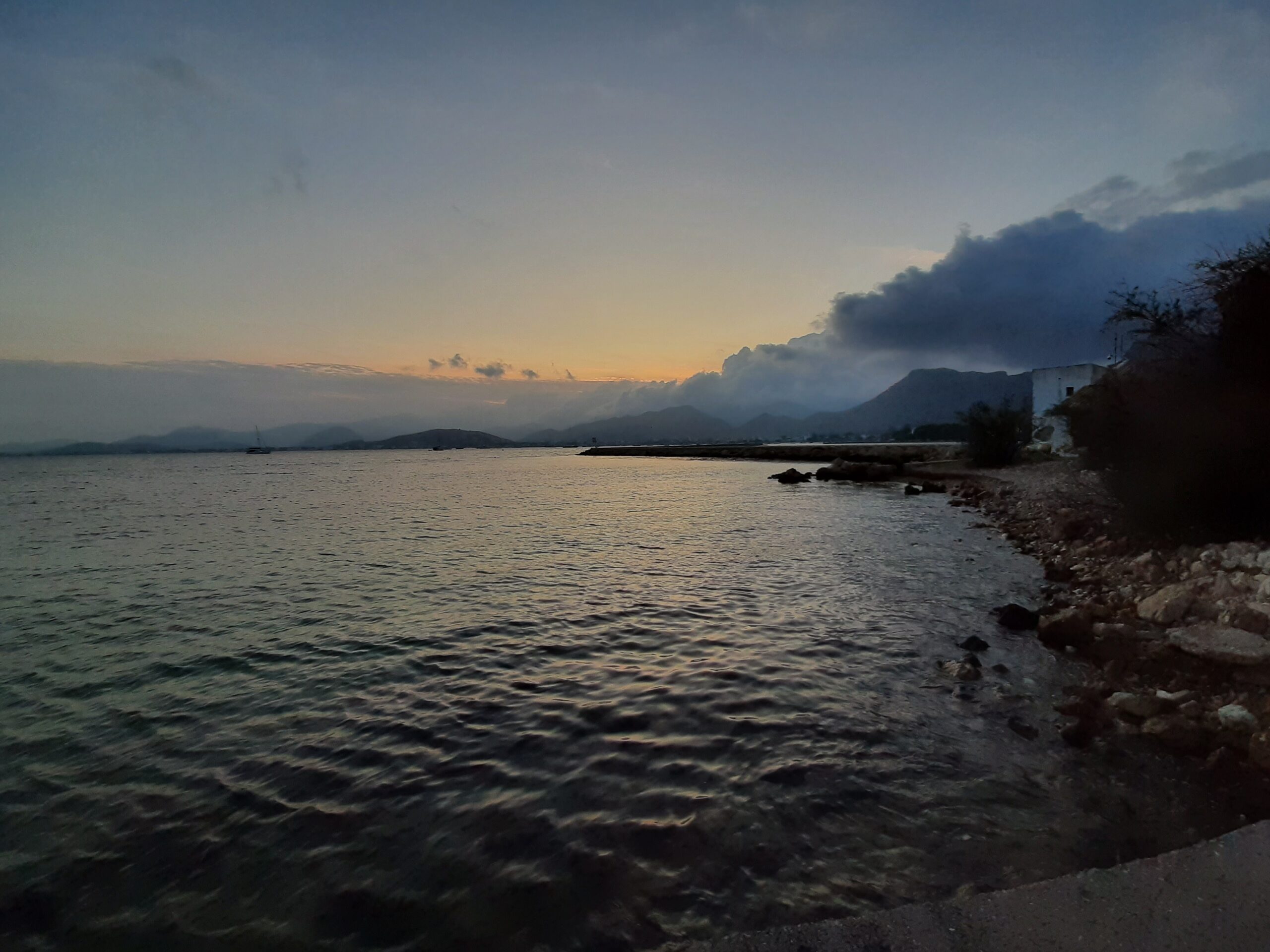 Het strand van Port de Pollença bij zonsondergang, met de ondiepe, kalme baai en de bergen op de achtergrond