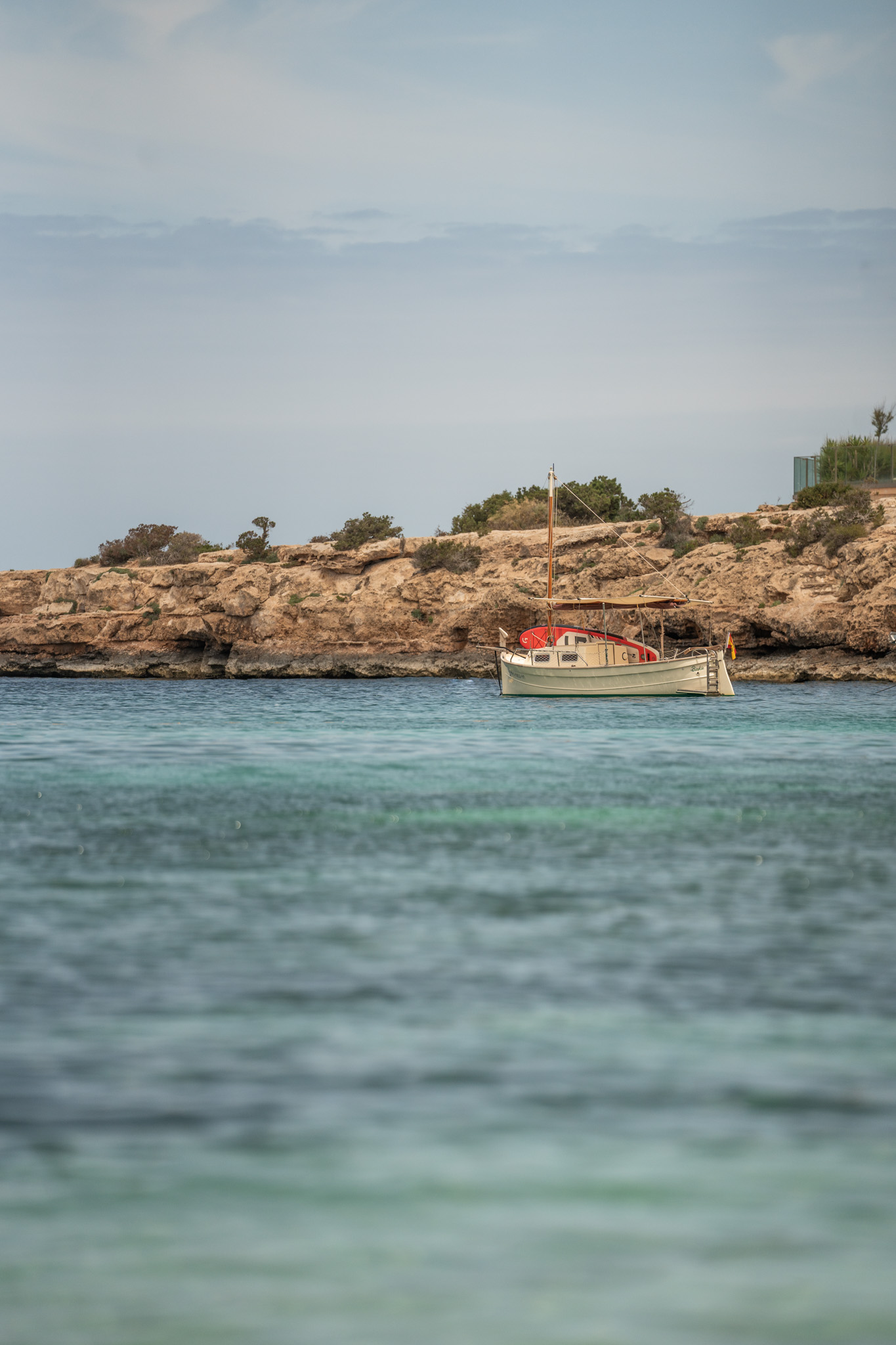 Ñora Beach Ibiza: strandrestaurant en ligbedden aan Port des Torrent 7 De baai van Port des Torrent met een bootje voor de rotsen