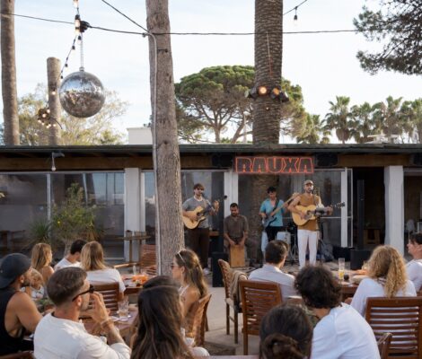 Het terras van Rauxa Ibiza met houten tafels, palmen en een discobal in de avond