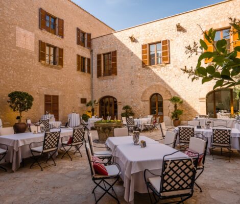De binnenplaats van restaurant Sa Clastra op landgoed Castell Son Claret op Mallorca, met gedekte tafels tussen honingkleurige muren