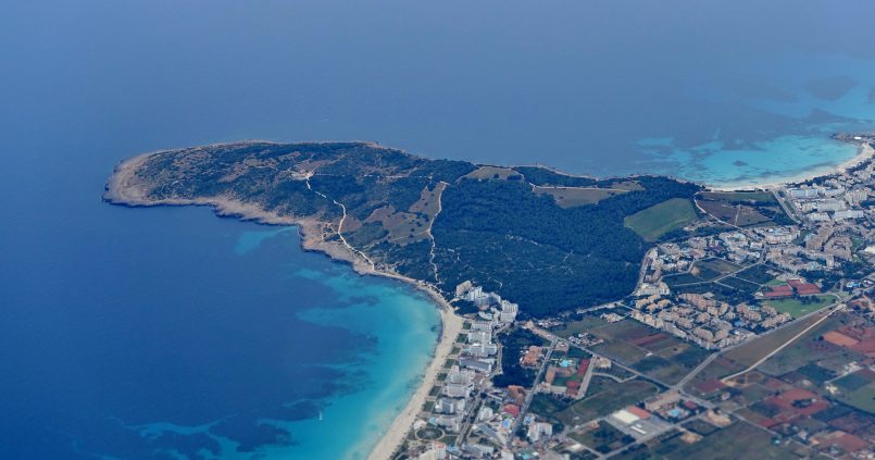 Luchtfoto van het strand van Sa Coma op Mallorca met turquoise ondiep water, de badplaats en het groene schiereiland Punta de n'Amer ernaast