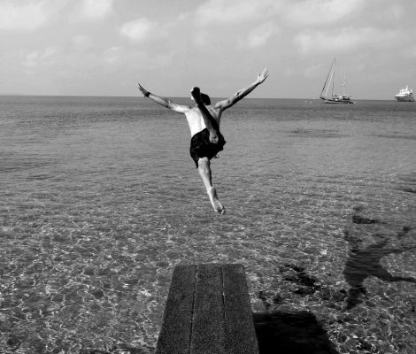 Zwart-witfoto van iemand die vanaf de houten vlonder van Sa Trinxa in het heldere water van Ses Salines springt