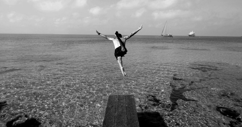 Zwart-witfoto van iemand die vanaf de houten vlonder van Sa Trinxa in het heldere water van Ses Salines springt