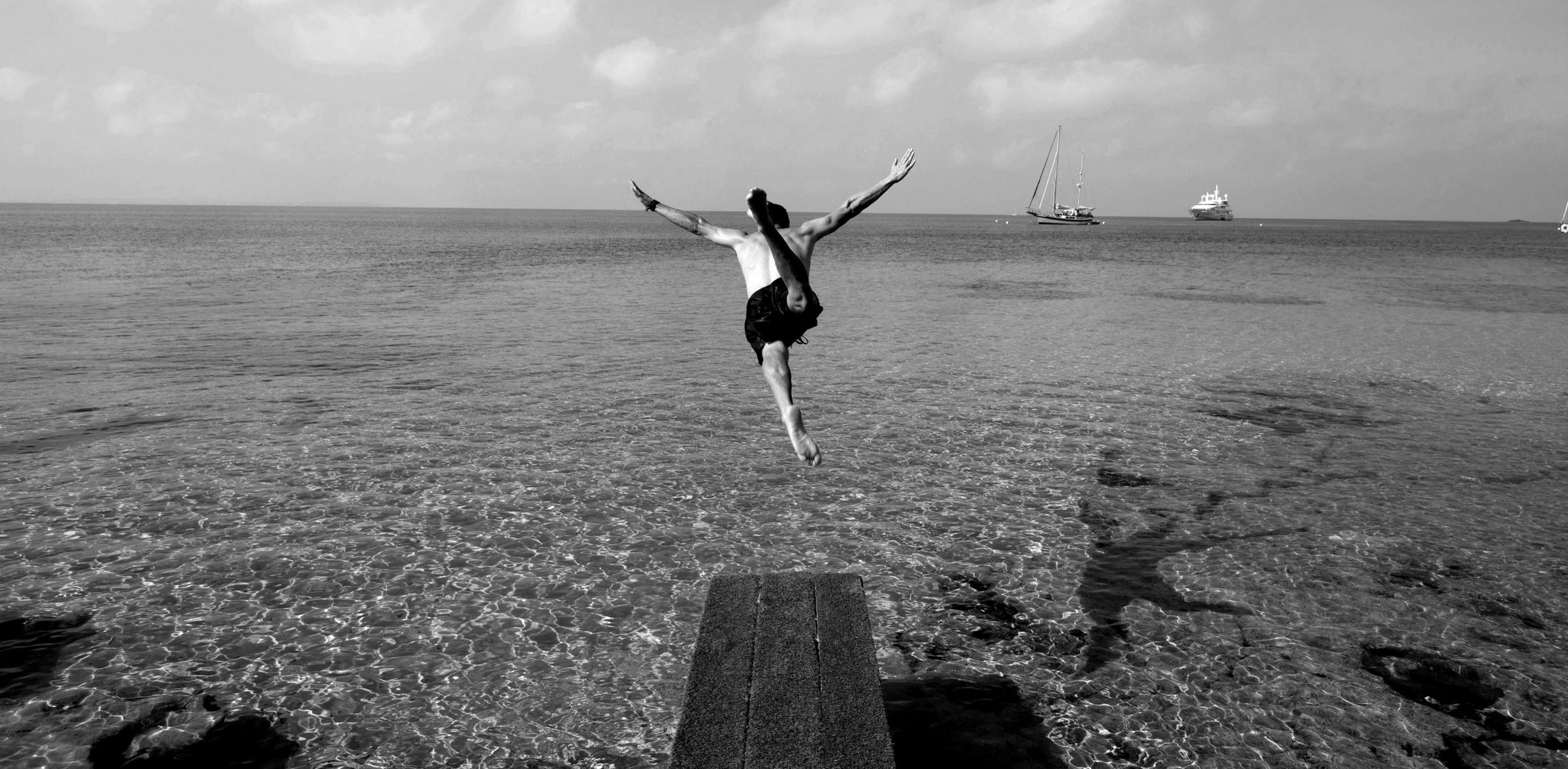 Zwart-witfoto van iemand die vanaf de houten vlonder van Sa Trinxa in het heldere water van Ses Salines springt