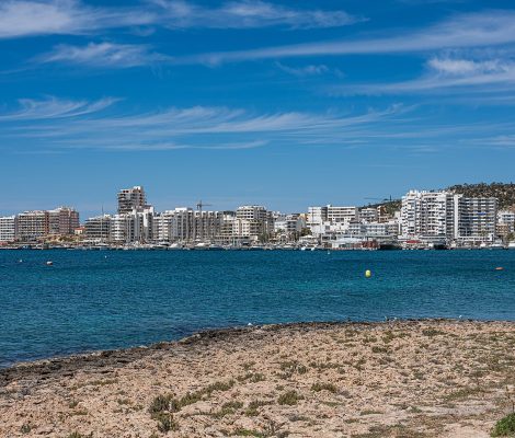 De baai van Sant Antoni op Ibiza met de skyline van de stad, helder blauw water en rotsen op de voorgrond
