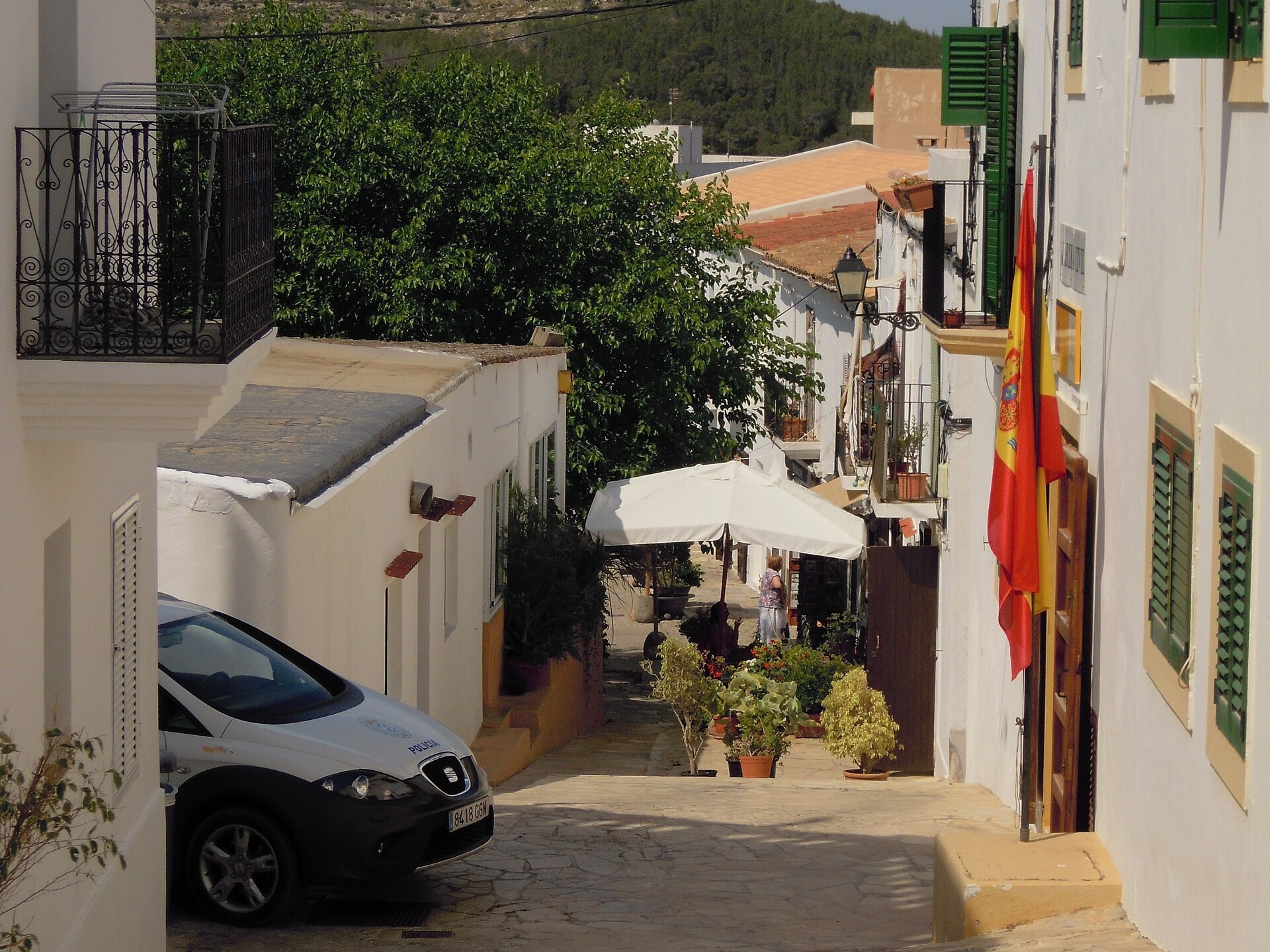 Wit straatje met groene luiken, bloempotten en een terras in het centrum van Sant Joan de Labritja