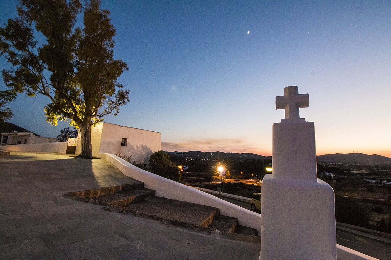 Avondlicht op het plein van de Puig de Missa in Santa Eulària des Riu, met het stenen kruis en uitzicht over het dal