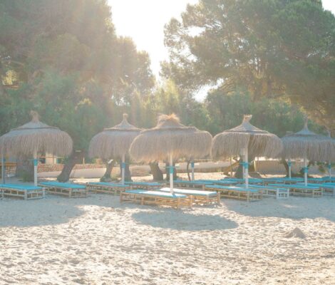 Rieten parasols en ligbedden op het zand van S'Arenal de Portocolom onder de pijnbomen
