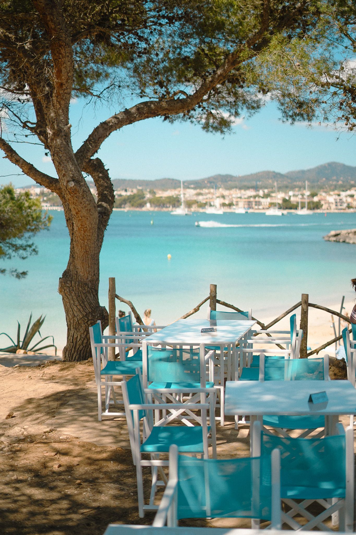 Blauwe tafels en stoelen op het terras van S'Arenal de Portocolom met zicht op de baai en de boten
