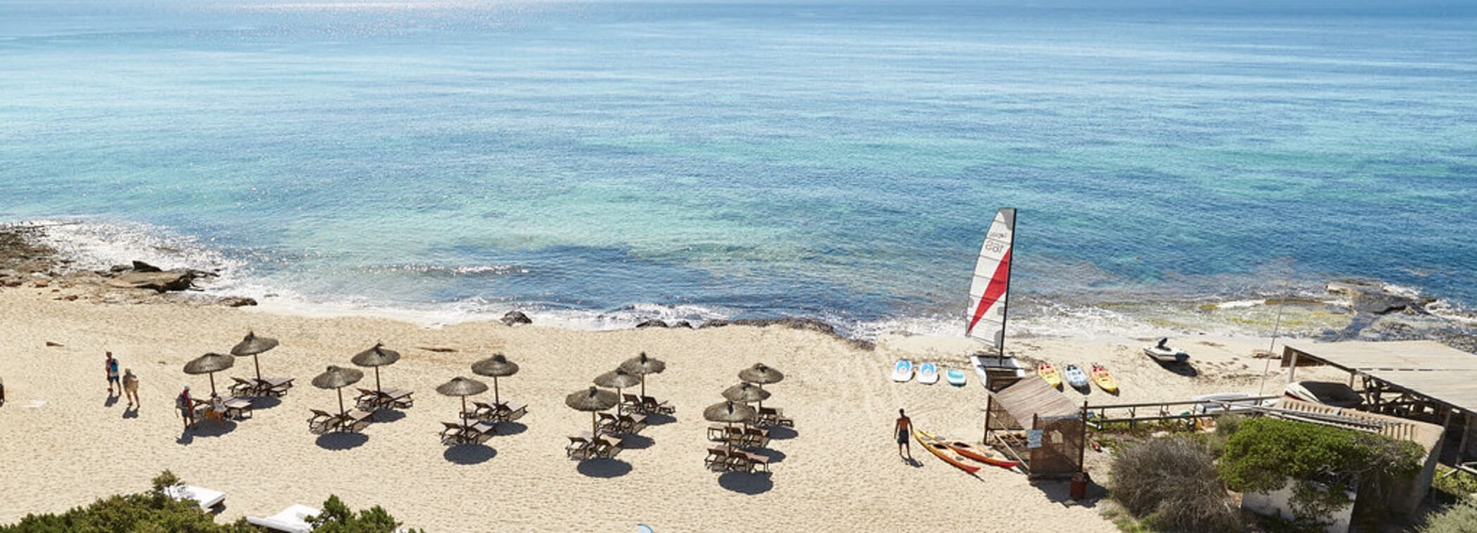Het strand voor South met parasols en ligbedden aan Platja de Migjorn
