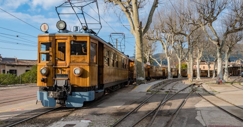 Het houten motorrijtuig nummer 1 van de trein van Sóller op het emplacement van het station van Sóller, onder kale platanen en een blauwe lucht