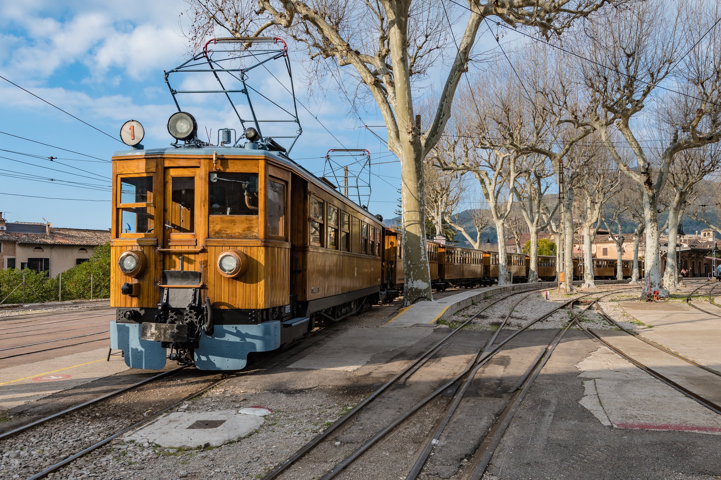 Trein Palma Sóller: het houten treintje door de bergen naar Sóller en de haven 1 Het houten motorrijtuig nummer 1 van de trein van Sóller op het emplacement van het station van Sóller, onder kale platanen en een blauwe lucht