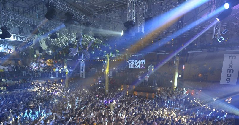Volle dansvloer van Amnesia Ibiza met lichtbundels onder het stalen dak